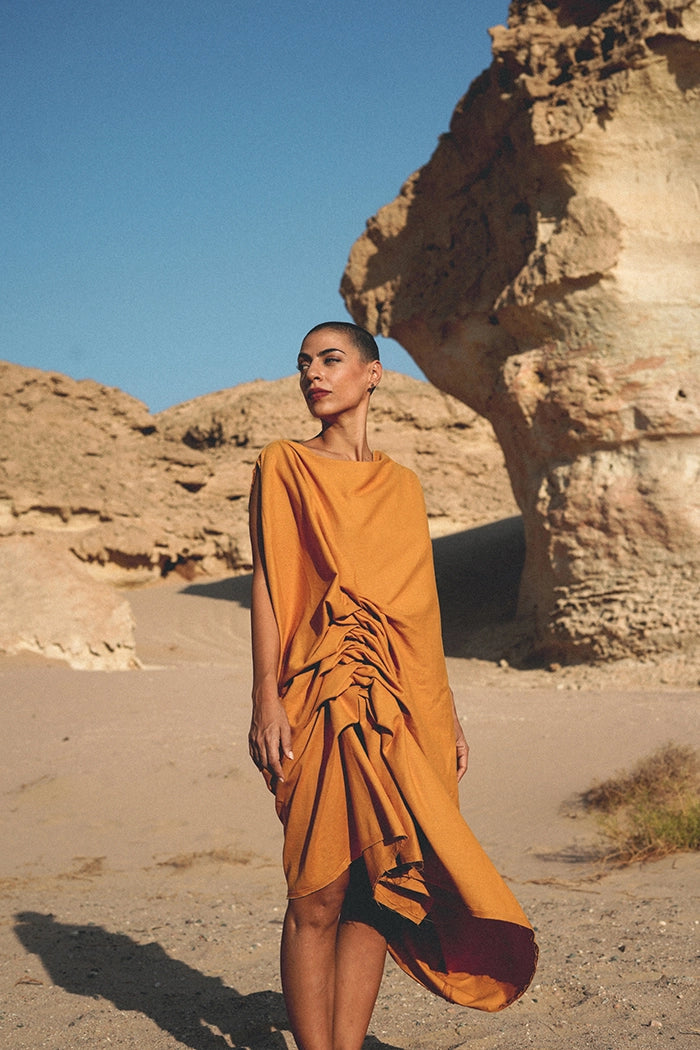 Model wearing an avant-garde draped dress by LARAKHOURY in a desert landscape.